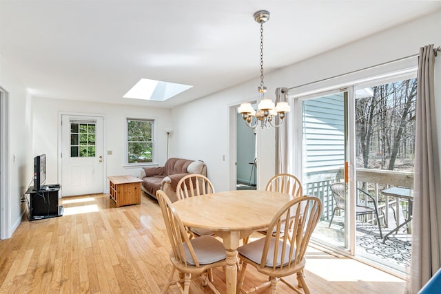 dining space with a skylight, a chandelier, and light wood-style floors