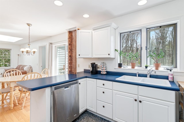 kitchen with dark countertops, dishwasher, a sink, a peninsula, and an inviting chandelier
