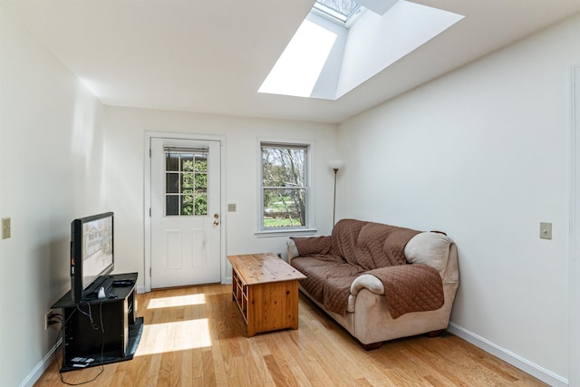 living room featuring a skylight, baseboards, and light wood finished floors