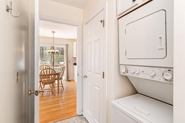 laundry room featuring laundry area, an inviting chandelier, and stacked washer and clothes dryer
