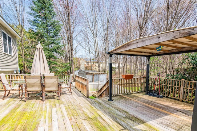wooden terrace featuring outdoor dining area, a storage shed, and an outbuilding