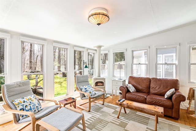 sunroom with ornamental molding, a wood stove, wood finished floors, and a wealth of natural light