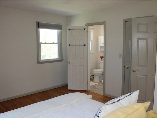bedroom with baseboards, ensuite bathroom, a baseboard heating unit, and wood finished floors
