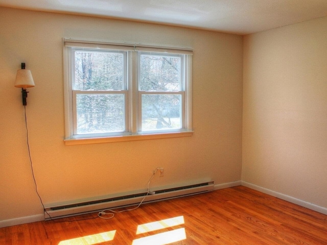 unfurnished room featuring baseboards, a baseboard heating unit, and wood finished floors