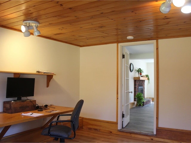 home office with a fireplace with raised hearth, baseboards, wooden ceiling, and wood finished floors