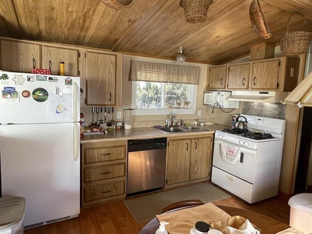 kitchen with a sink, white appliances, light countertops, wooden ceiling, and range hood
