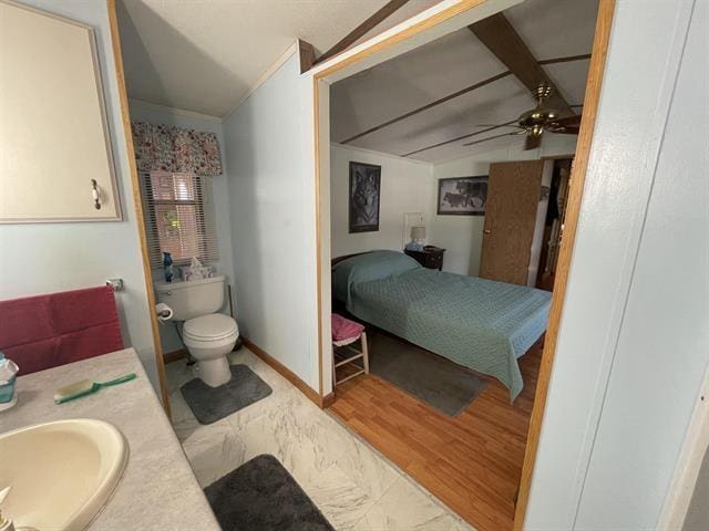 ensuite bathroom featuring ceiling fan, a sink, ensuite bath, toilet, and vaulted ceiling
