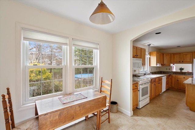 kitchen featuring pendant lighting, arched walkways, brown cabinets, a sink, and white appliances