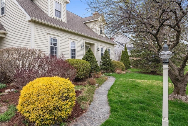 view of side of home with a yard and a shingled roof