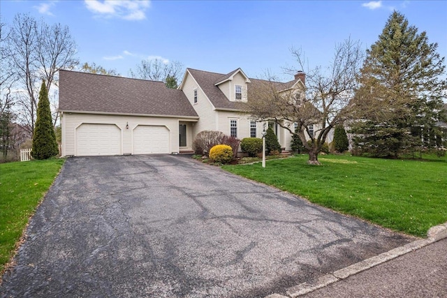 new england style home featuring aphalt driveway, a front yard, roof with shingles, a chimney, and an attached garage