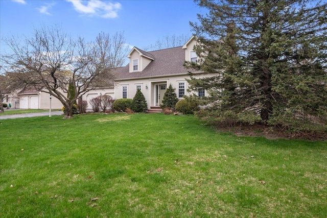 new england style home featuring an attached garage, roof with shingles, a front yard, and concrete driveway