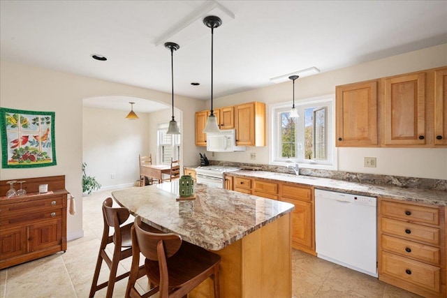 kitchen featuring light stone counters, white appliances, arched walkways, a kitchen bar, and a kitchen island