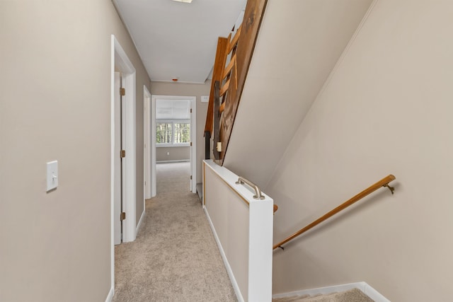 corridor featuring baseboards, an upstairs landing, and light carpet