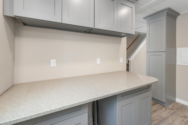 kitchen featuring light stone counters, open shelves, light wood finished floors, and gray cabinetry