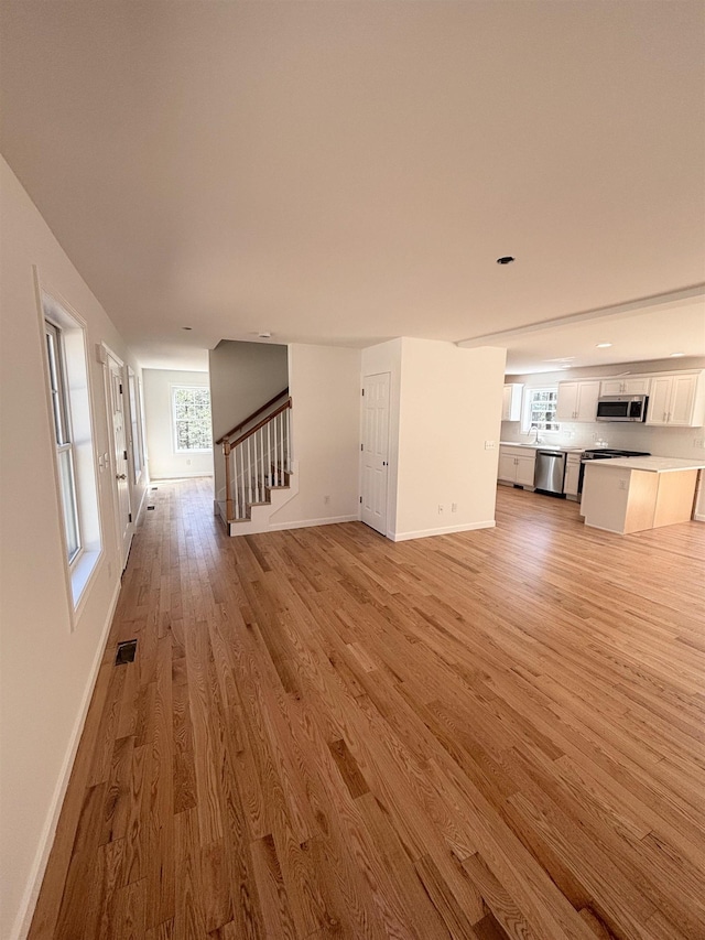 unfurnished living room featuring baseboards, visible vents, stairway, and light wood-type flooring