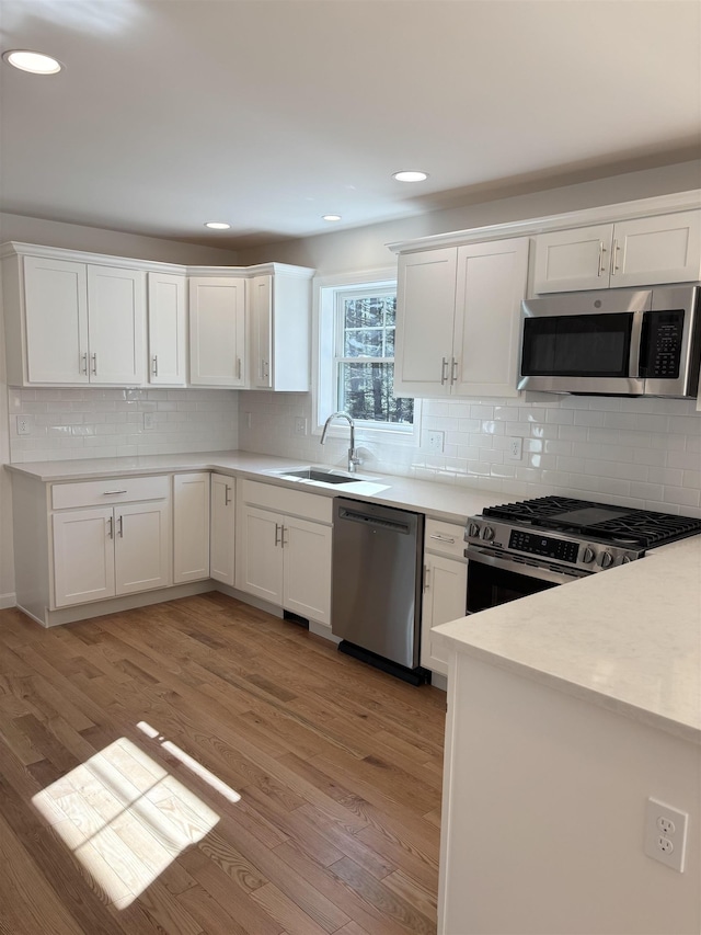 kitchen with backsplash, appliances with stainless steel finishes, a sink, and light wood-type flooring