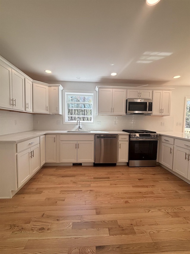 kitchen featuring a sink, decorative backsplash, stainless steel appliances, and light wood-style flooring