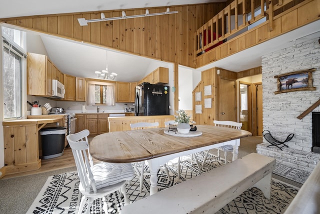 dining space with a chandelier, wood walls, light colored carpet, and plenty of natural light