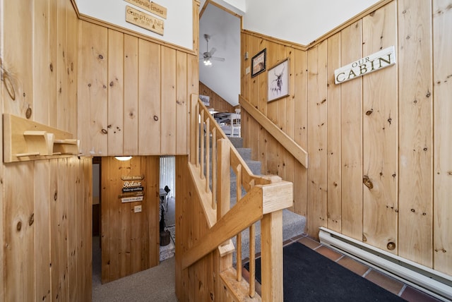 stairs featuring carpet flooring, a ceiling fan, wood walls, and a baseboard heating unit
