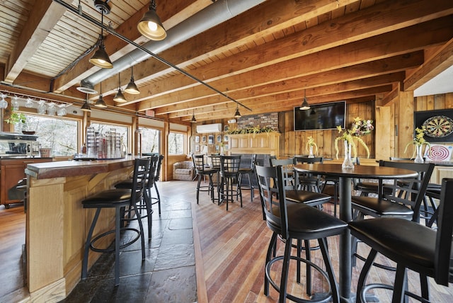 dining room with indoor bar, wood walls, beam ceiling, and dark wood-type flooring
