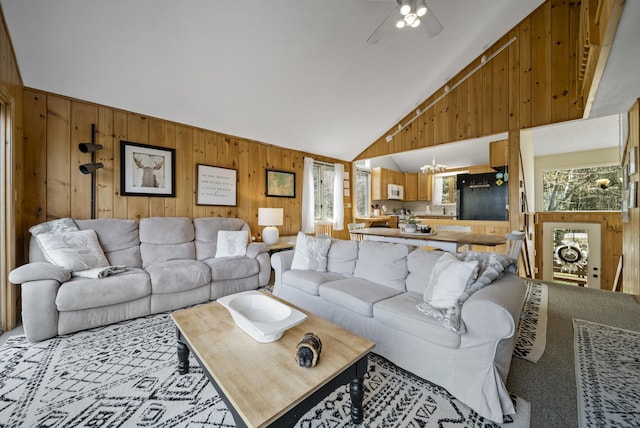 carpeted living area featuring a ceiling fan, wooden walls, and high vaulted ceiling
