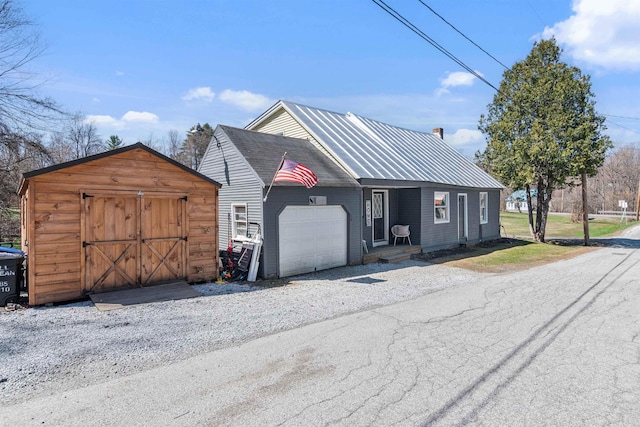 chalet / cabin featuring a garage, a chimney, metal roof, a storage shed, and an outbuilding
