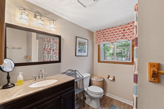 bathroom with a textured ceiling, tasteful backsplash, wood finished floors, vanity, and toilet