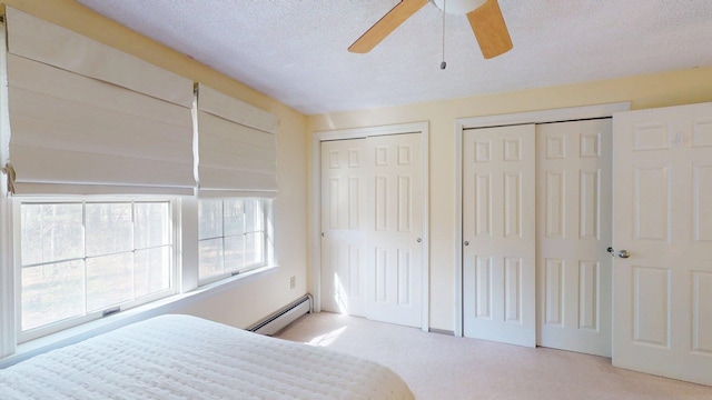 carpeted bedroom with a textured ceiling, multiple closets, ceiling fan, and a baseboard heating unit