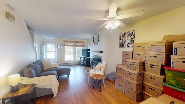 living area with ceiling fan, a glass covered fireplace, and wood finished floors