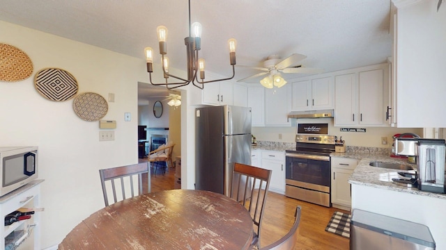 kitchen with ceiling fan with notable chandelier, white cabinets, stainless steel appliances, and under cabinet range hood