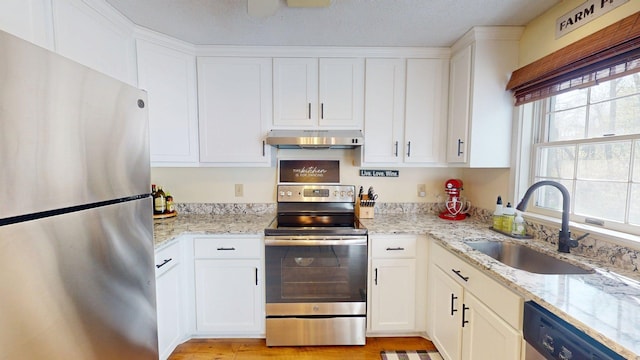 kitchen featuring appliances with stainless steel finishes, a sink, light stone counters, white cabinets, and under cabinet range hood
