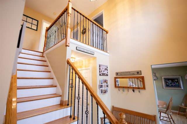 stairs featuring baseboards, wood finished floors, and a towering ceiling