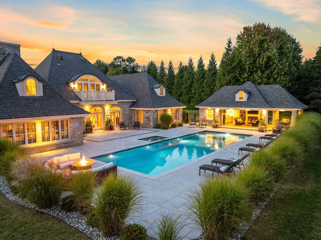 pool at dusk featuring an outdoor structure, a pool with connected hot tub, a patio, an exterior structure, and a fire pit