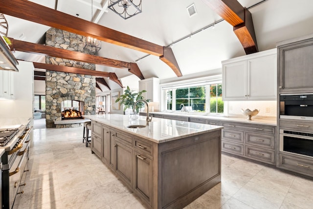 kitchen featuring light stone counters, beam ceiling, a sink, a stone fireplace, and visible vents