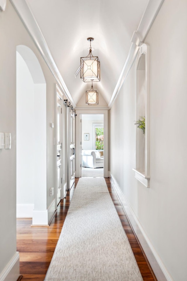 hallway featuring arched walkways, baseboards, vaulted ceiling, and dark wood-type flooring
