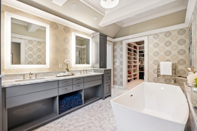 bathroom with double vanity, a walk in closet, crown molding, a sink, and wallpapered walls
