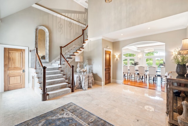 entrance foyer with crown molding, baseboards, a high ceiling, stairway, and arched walkways