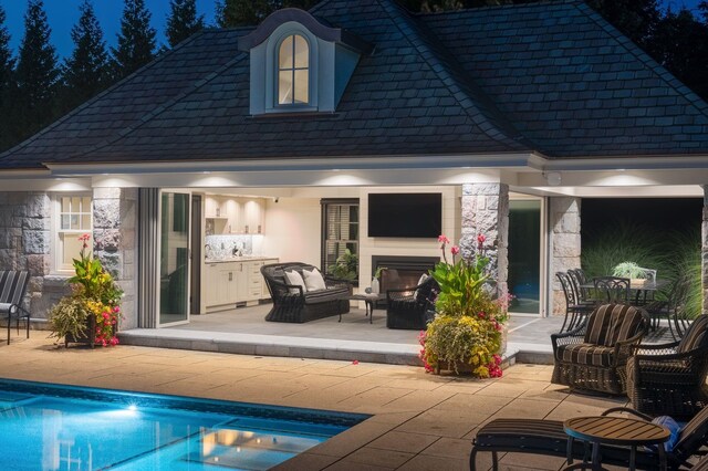 rear view of house featuring an outdoor pool, an exterior structure, an outdoor hangout area, a patio, and stone siding