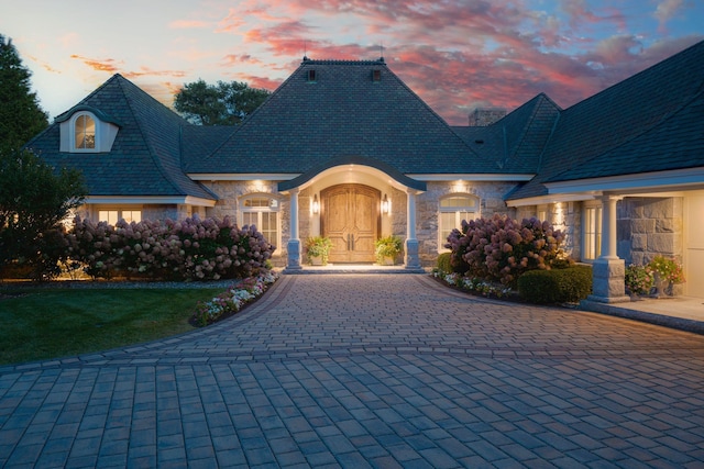 view of front of home with decorative driveway, a high end roof, and stone siding