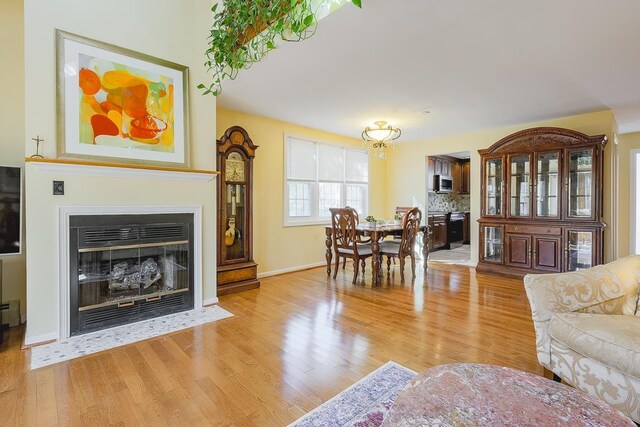 living area with a fireplace with flush hearth, baseboards, a baseboard radiator, and light wood-style flooring
