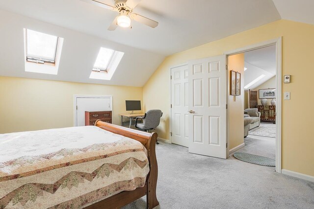 bedroom featuring vaulted ceiling with skylight, baseboards, light carpet, and a ceiling fan