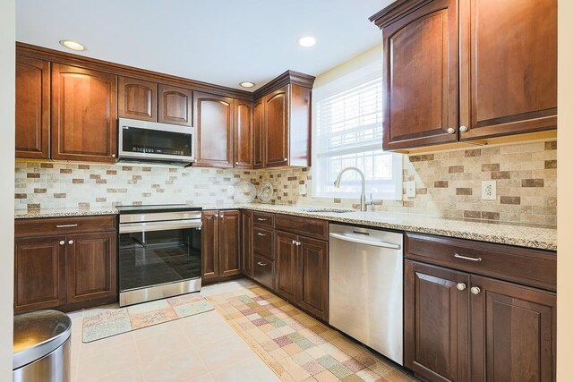 kitchen featuring backsplash, appliances with stainless steel finishes, a sink, and light stone counters