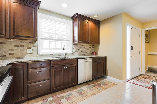 kitchen with tasteful backsplash, light stone countertops, dishwasher, a sink, and baseboards