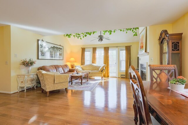 living area with a fireplace, baseboards, baseboard heating, light wood-type flooring, and a ceiling fan