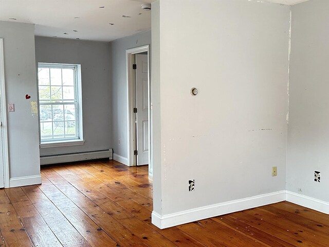 spare room with baseboards, wood-type flooring, and a baseboard heating unit
