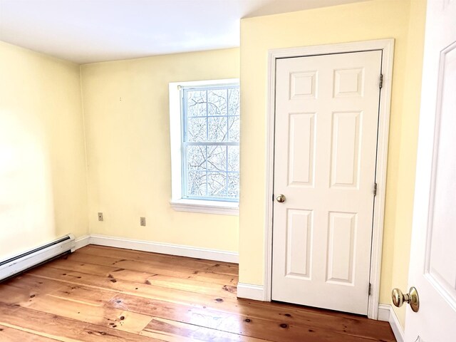 unfurnished room with wood-type flooring, a baseboard radiator, and baseboards