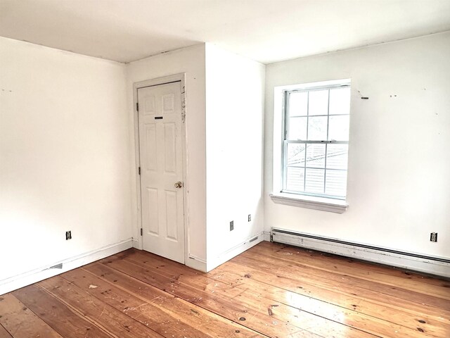 unfurnished room with baseboards, a baseboard heating unit, and hardwood / wood-style floors