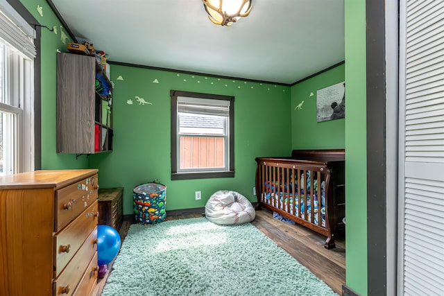 bedroom with a nursery area, baseboards, and wood finished floors