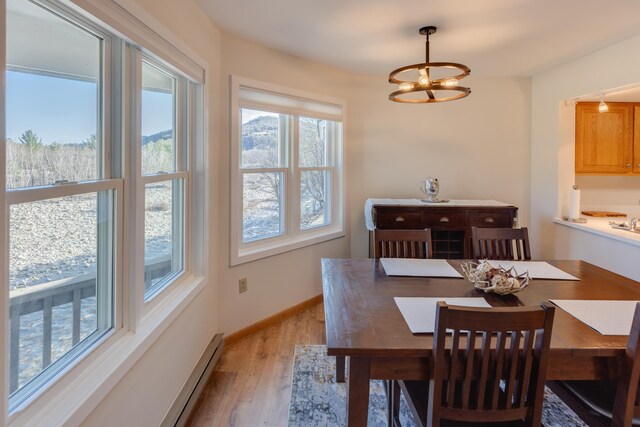 dining area with baseboards, a baseboard heating unit, light wood-style flooring, and an inviting chandelier