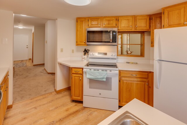 kitchen featuring light countertops, baseboards, white appliances, and light wood-style flooring